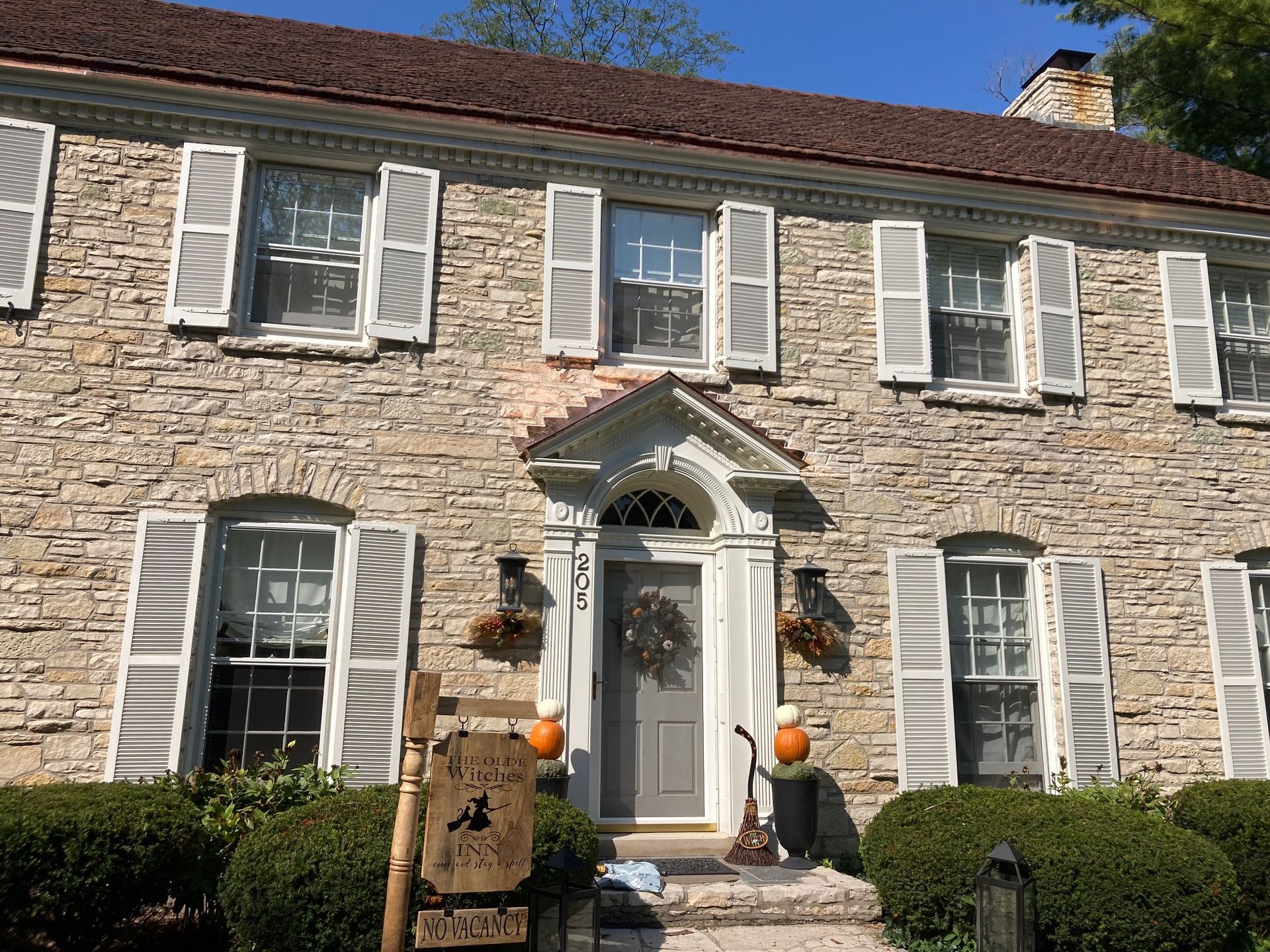 A large stone house with white shutters and pumpkins in front of it