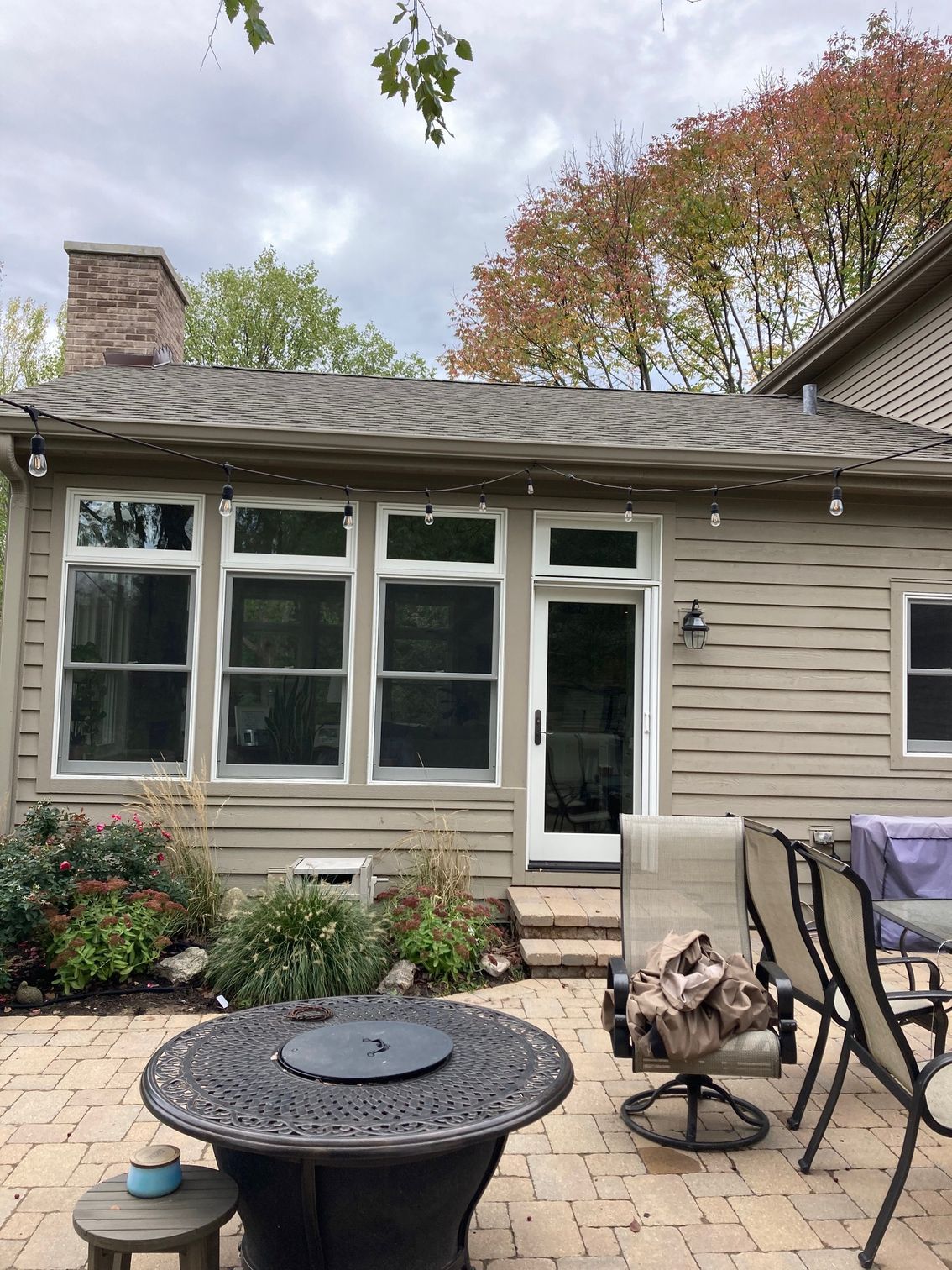 A patio with a fire pit and chairs in front of a house.