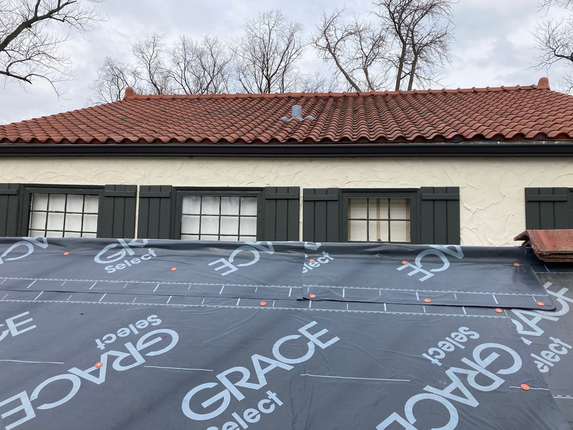 A house with a red tile roof and black shutters is being remodeled.