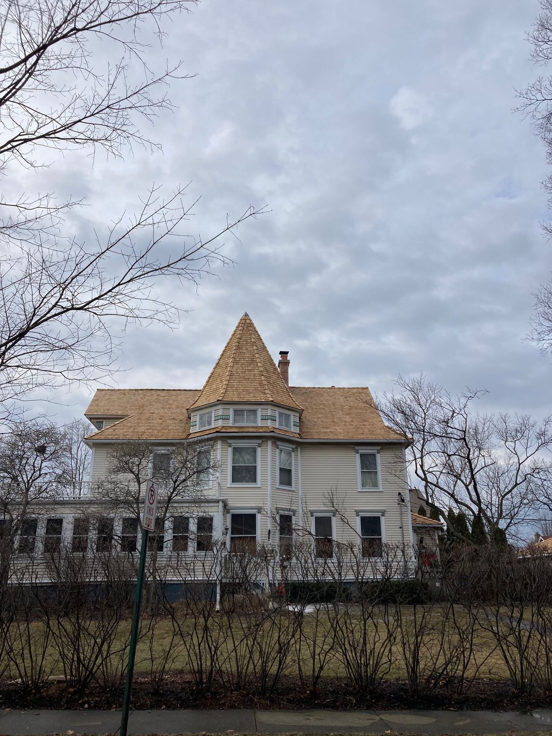 A large white house with a wooden roof is surrounded by trees and bushes.