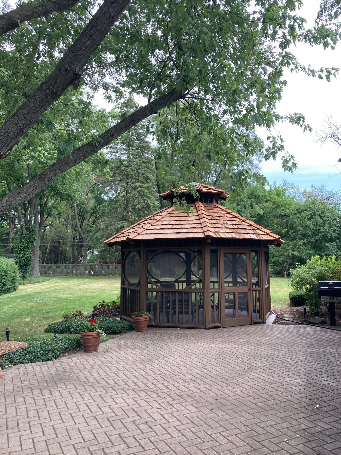 A gazebo is sitting on top of a brick patio next to a lush green field.