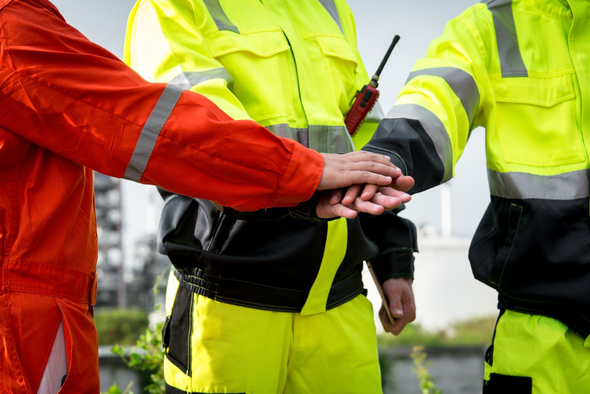 Workers in safety vests, hands together in a show of teamwork.