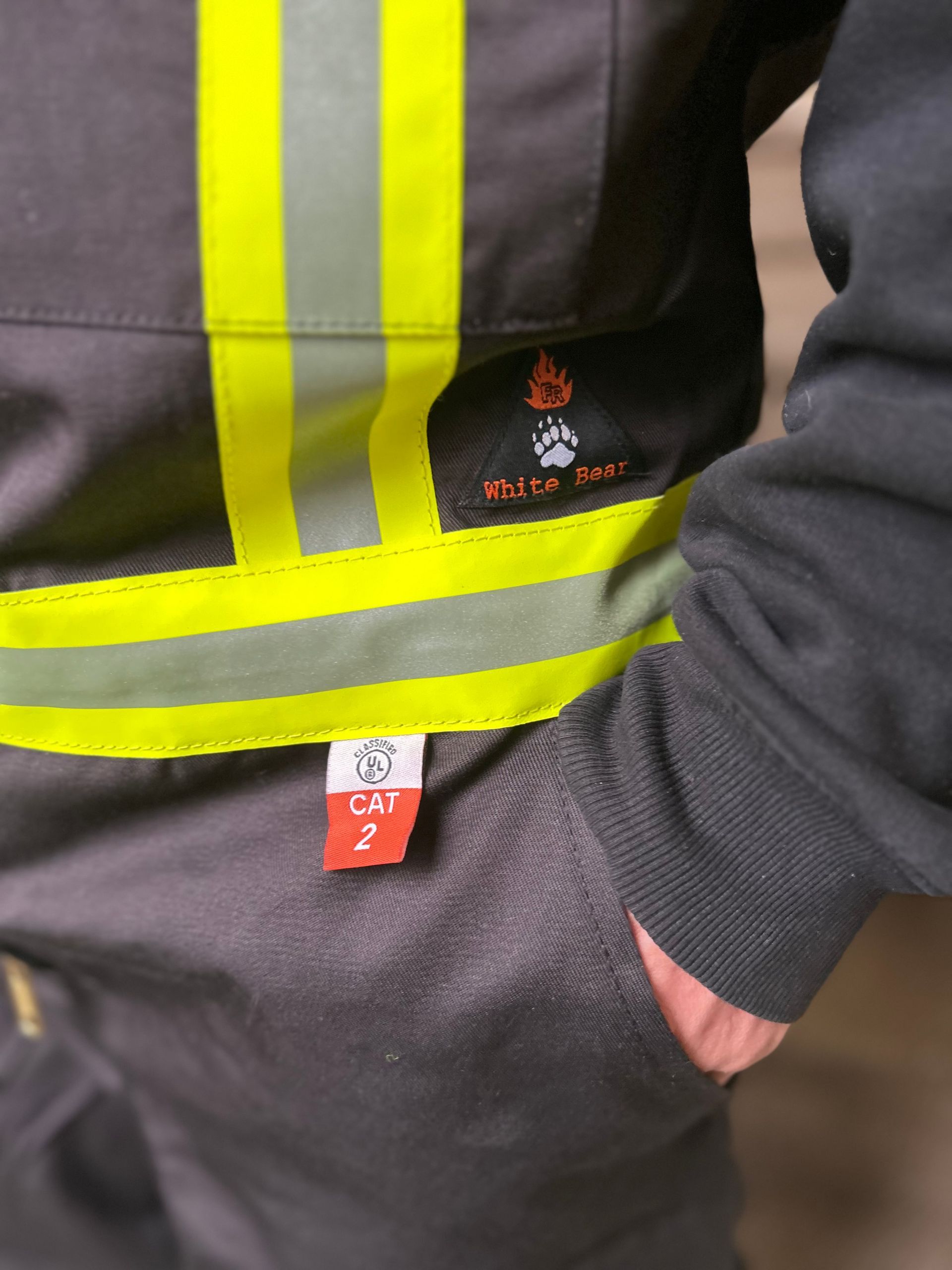 Fire-resistant workwear with reflective strips and a CAT 2 safety rating tag on a pocket.