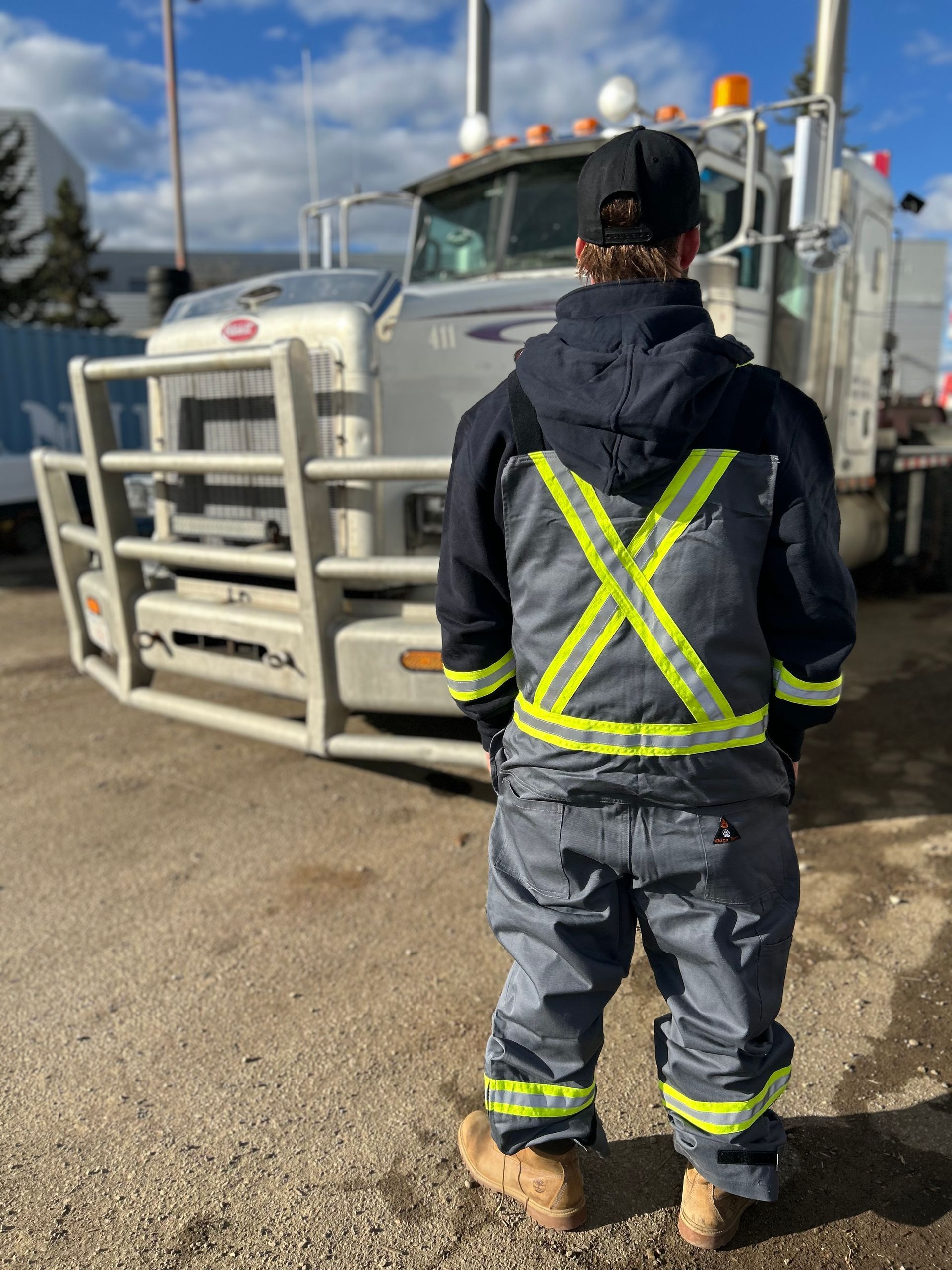 Person wearing safety gear, standing in front of a truck. The person's back is to the camera.