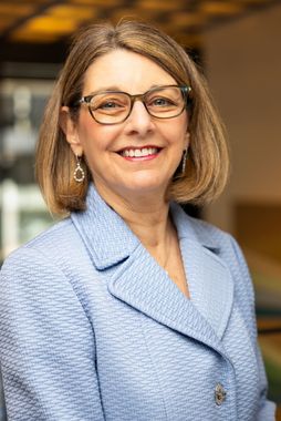 A woman wearing glasses and a blue jacket is smiling for the camera.