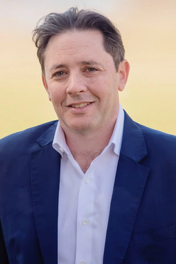 A man in a blue suit and white shirt is smiling for the camera.