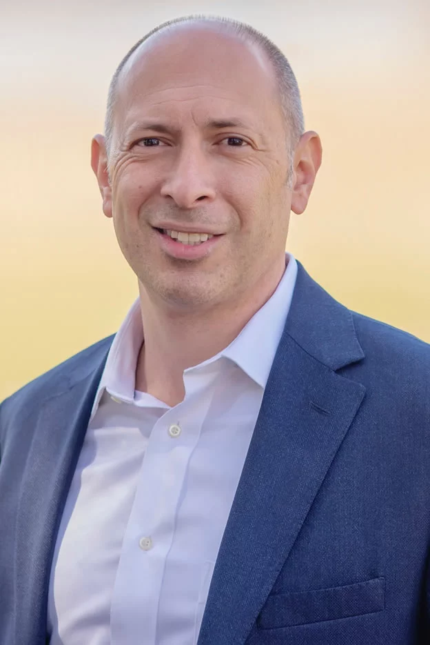 A man in a blue shirt and black pants is standing with his hands in his pockets.