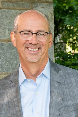 A man wearing glasses and a suit is smiling for the camera.