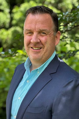 A man in a suit and blue shirt is smiling for the camera.