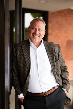 A man in a suit is leaning against a wall and smiling.