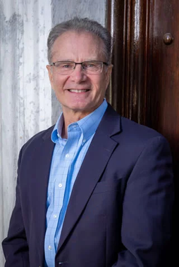 A man in a suit and blue shirt is standing in front of a door.