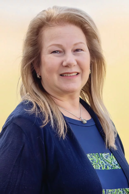 A woman wearing a blue sweater and a blue shirt is smiling for the camera.