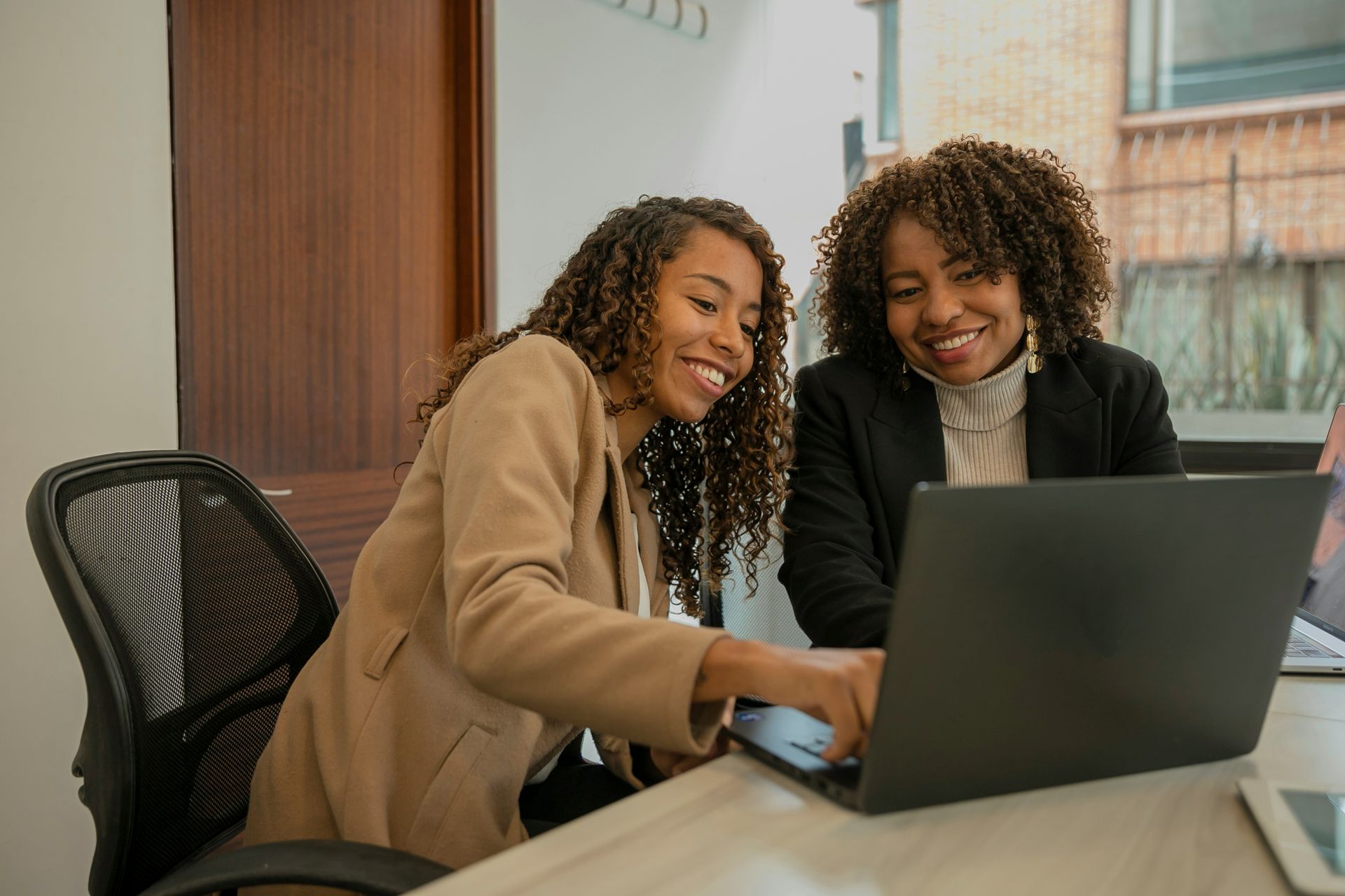 Three women are standing around a table looking at a laptop computer.