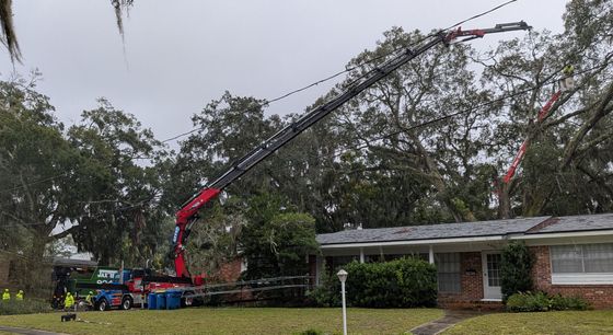 A crane removing a tree from above a house on a cloudy day.
