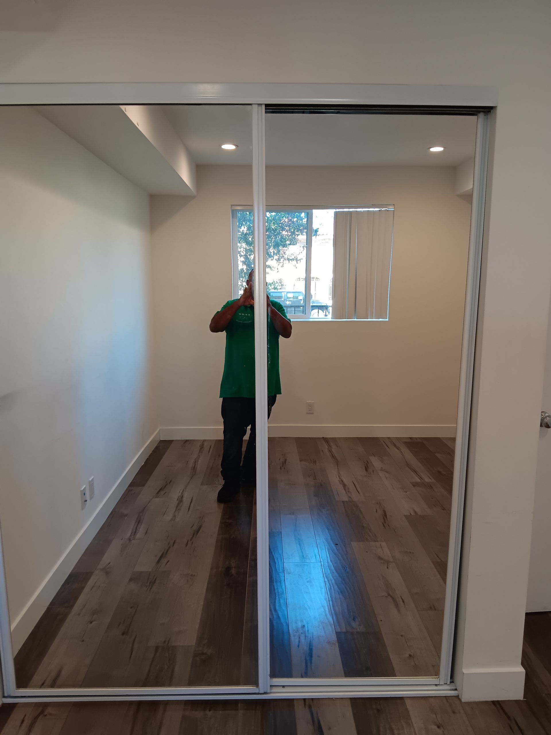 A man in a green shirt is standing in front of a sliding glass door.