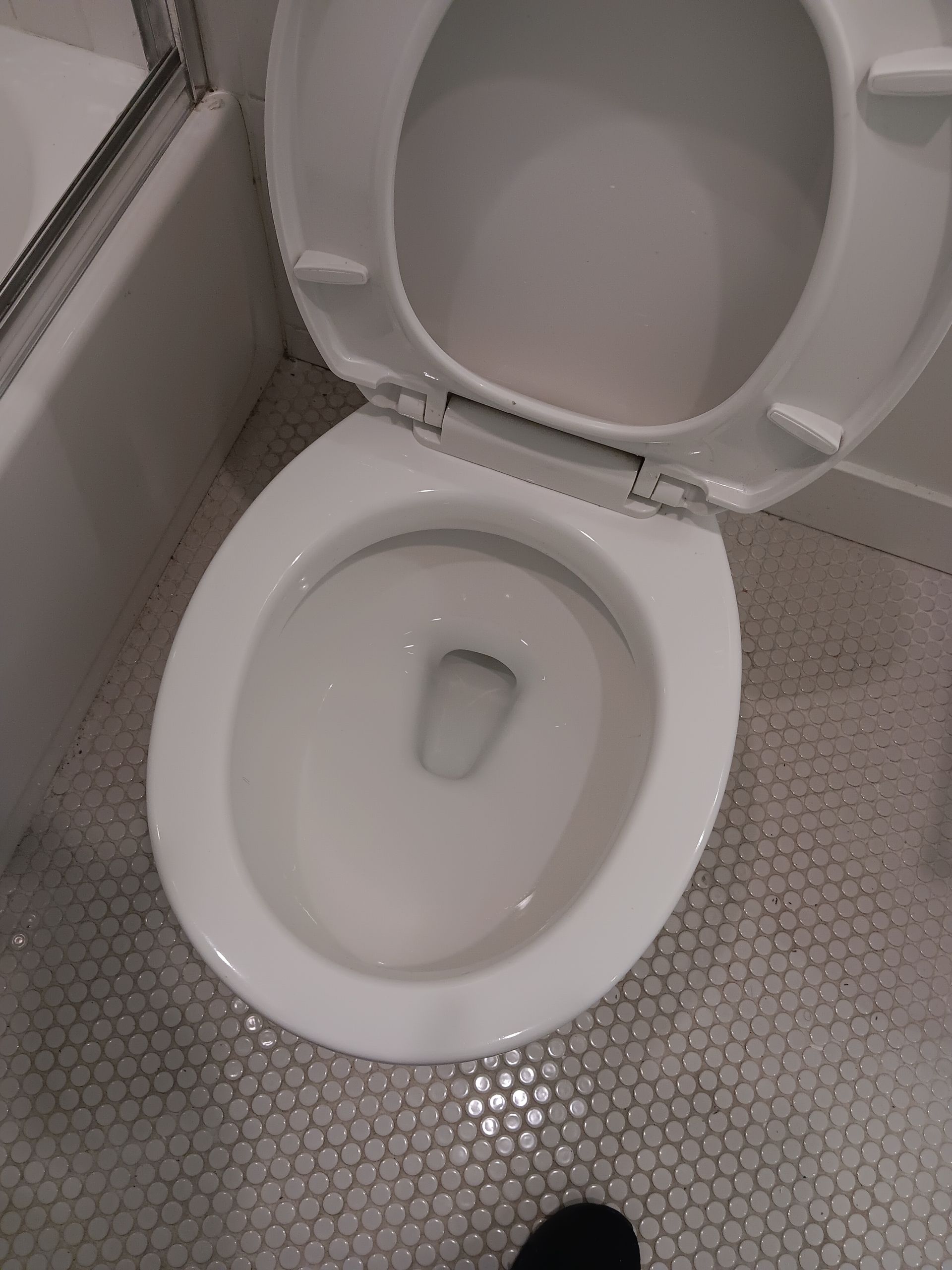 A white toilet is sitting on a tiled floor in a bathroom.