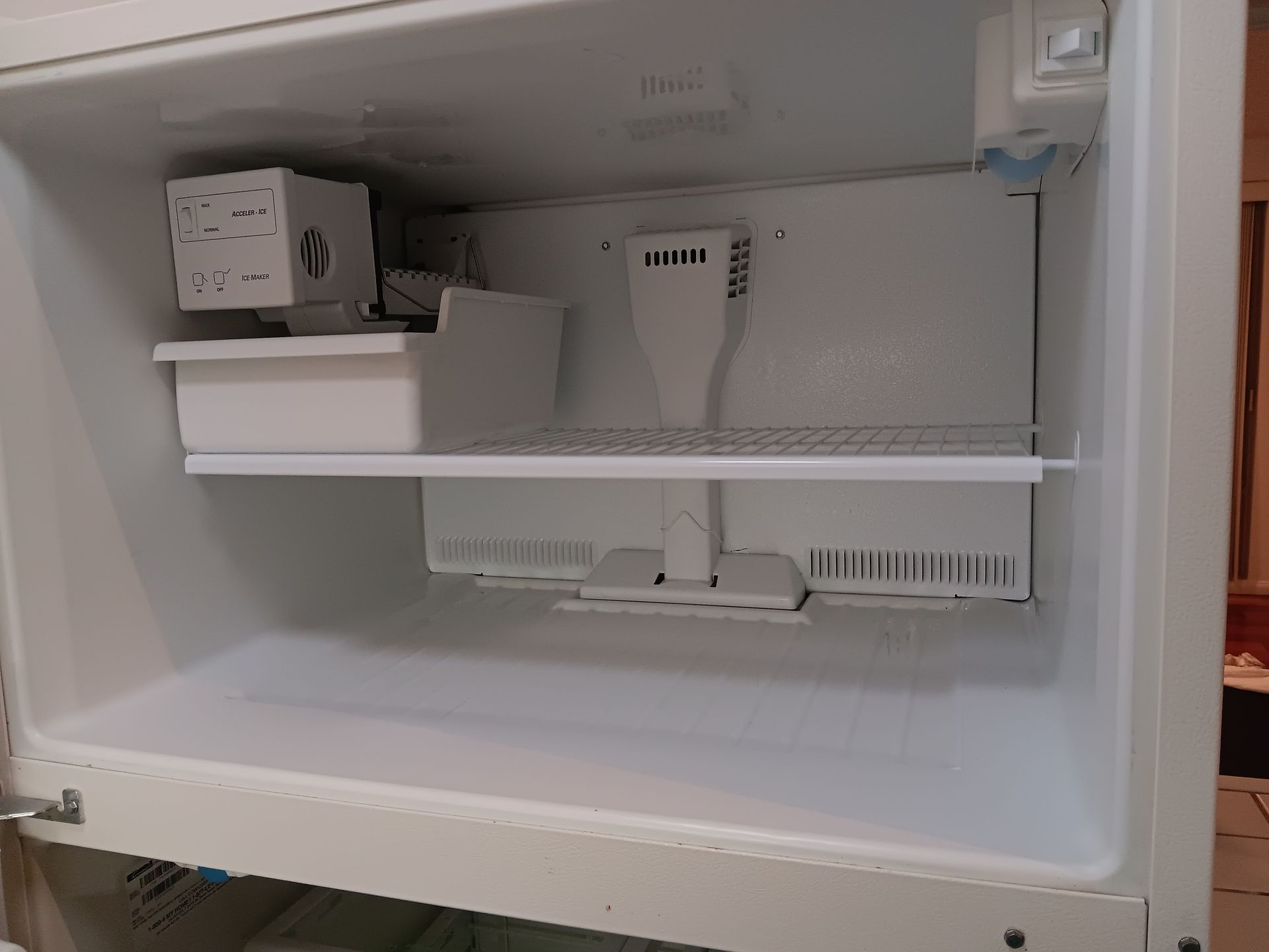 The inside of an empty refrigerator with a shelf and ice maker.