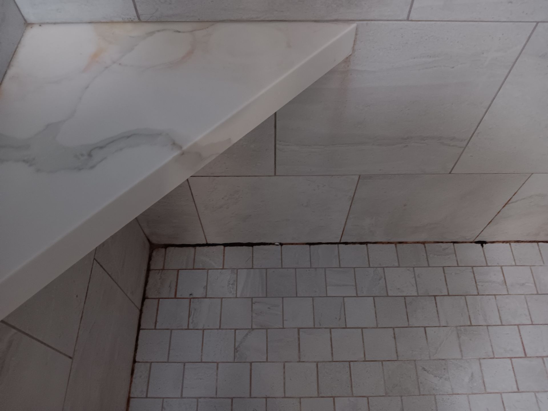 A corner of a bathroom with white tiles and a marble shelf.