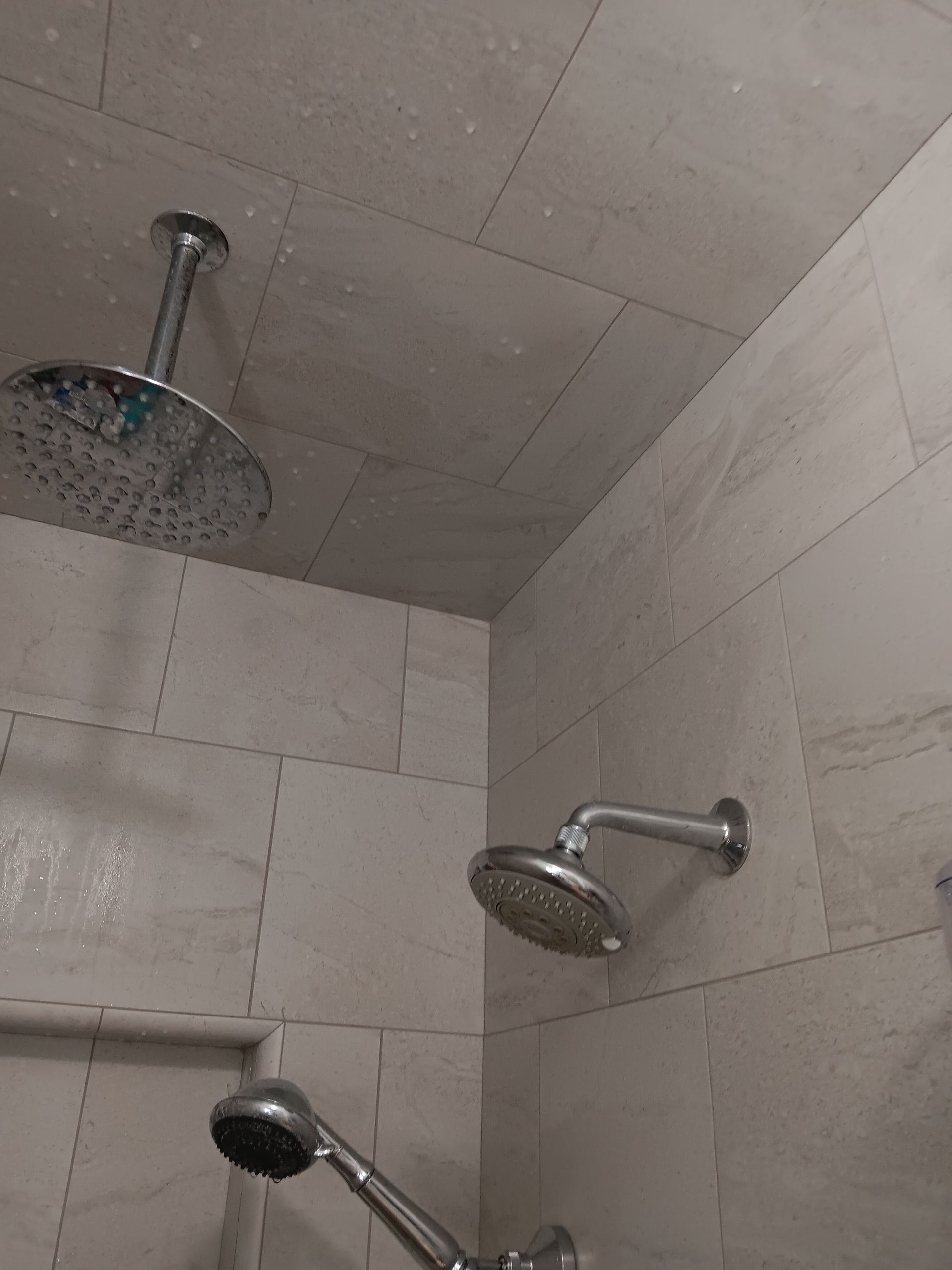 Two shower heads are hanging from the ceiling in a bathroom.