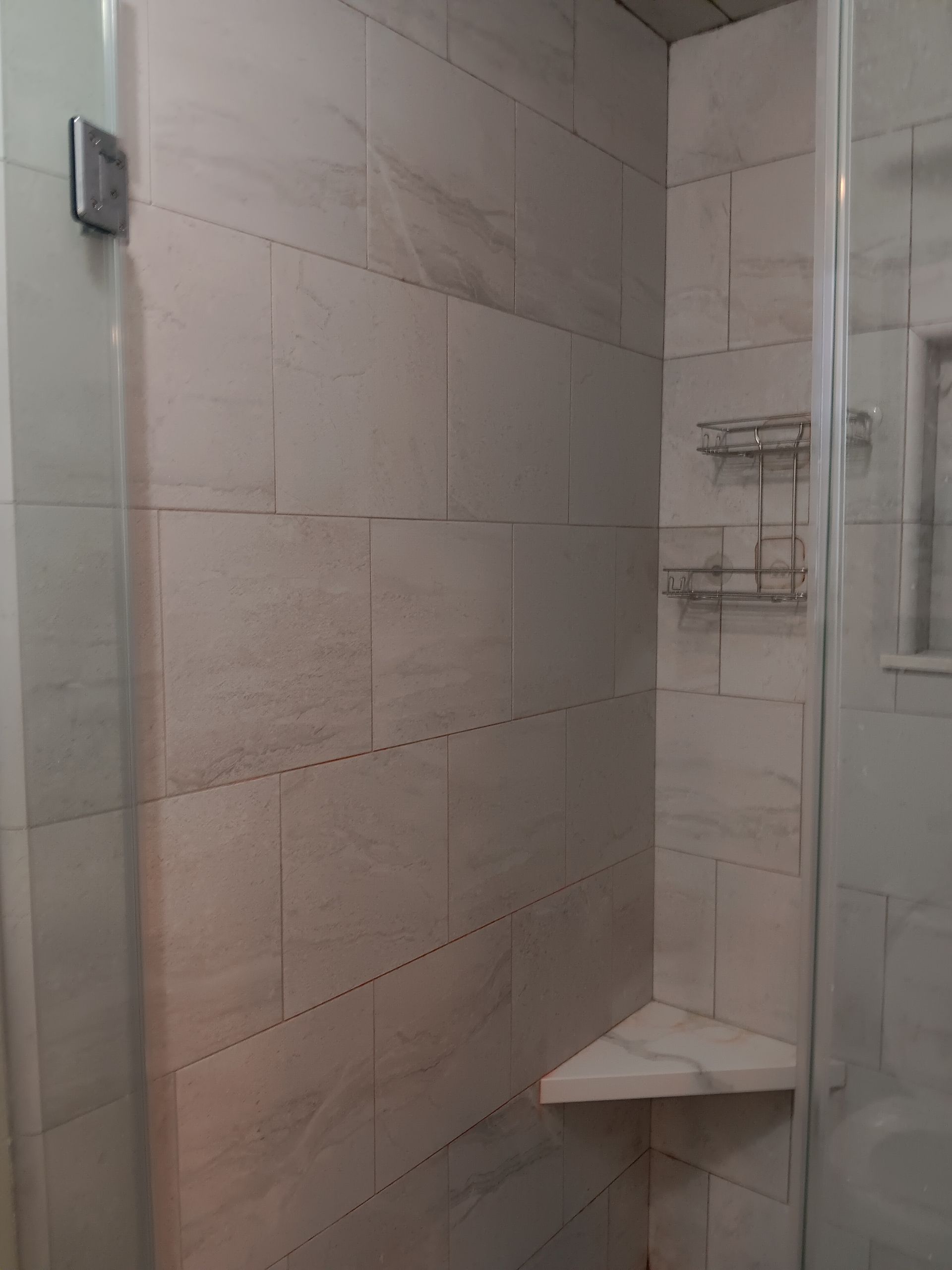 A bathroom with a walk in shower and a corner shelf.