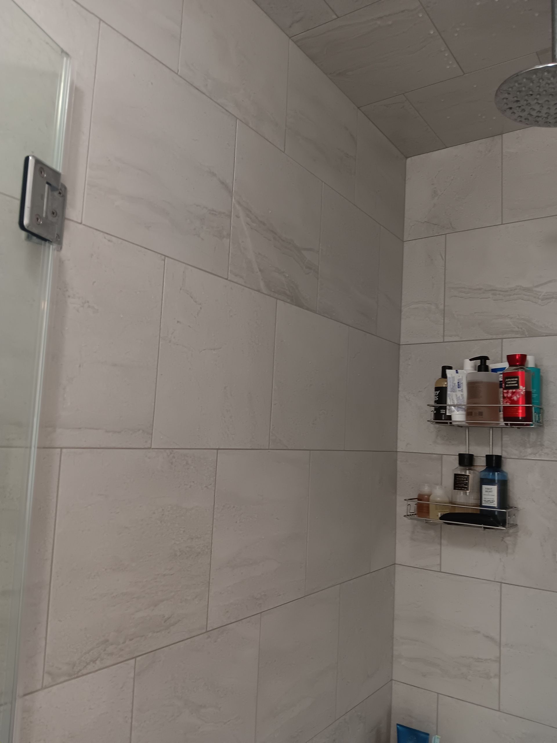 A bathroom with a shower head and a shelf with shampoo on it.
