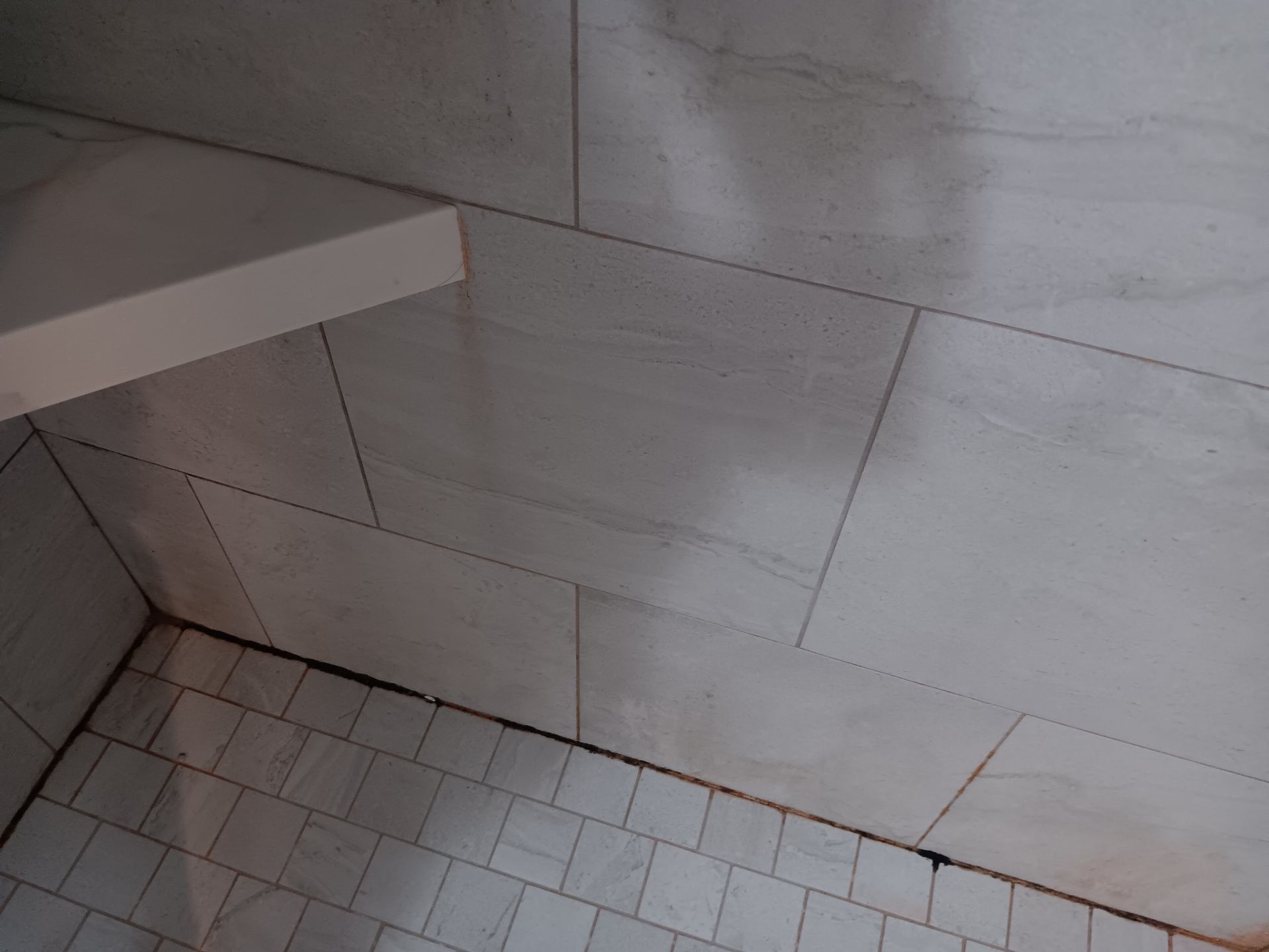 A bathroom with white tiles and a shelf in the corner