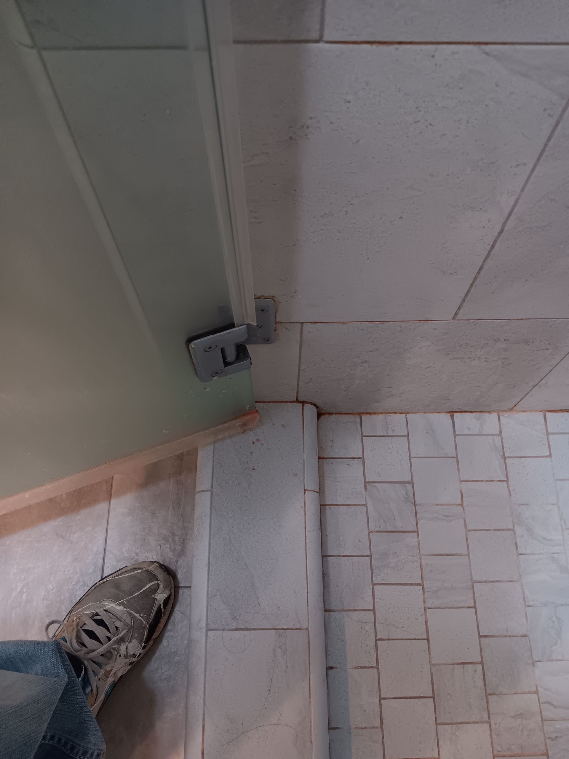 A person 's foot is standing on a tiled floor next to a door.