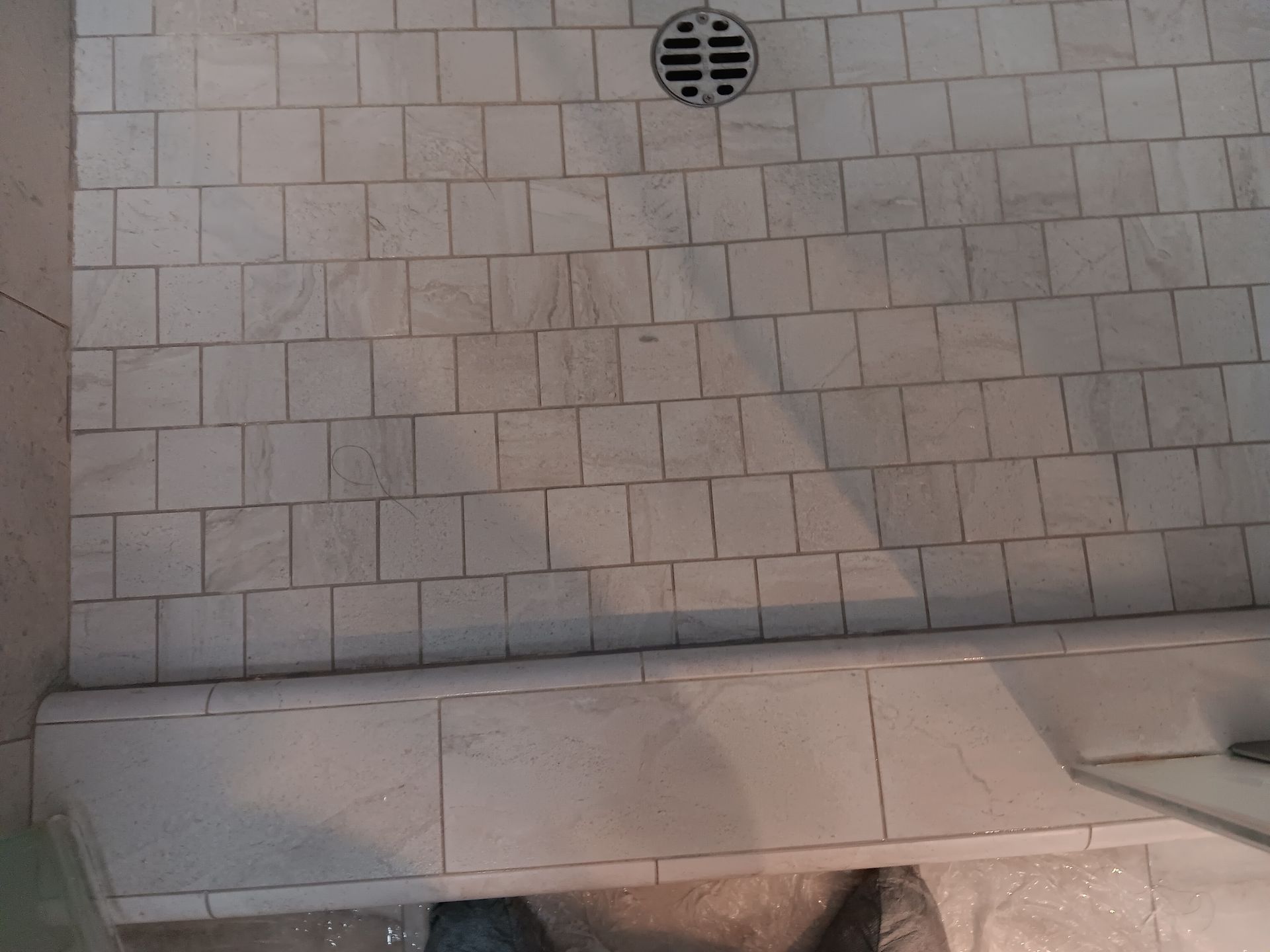 A shower stall with white tiles and a drain on the floor.