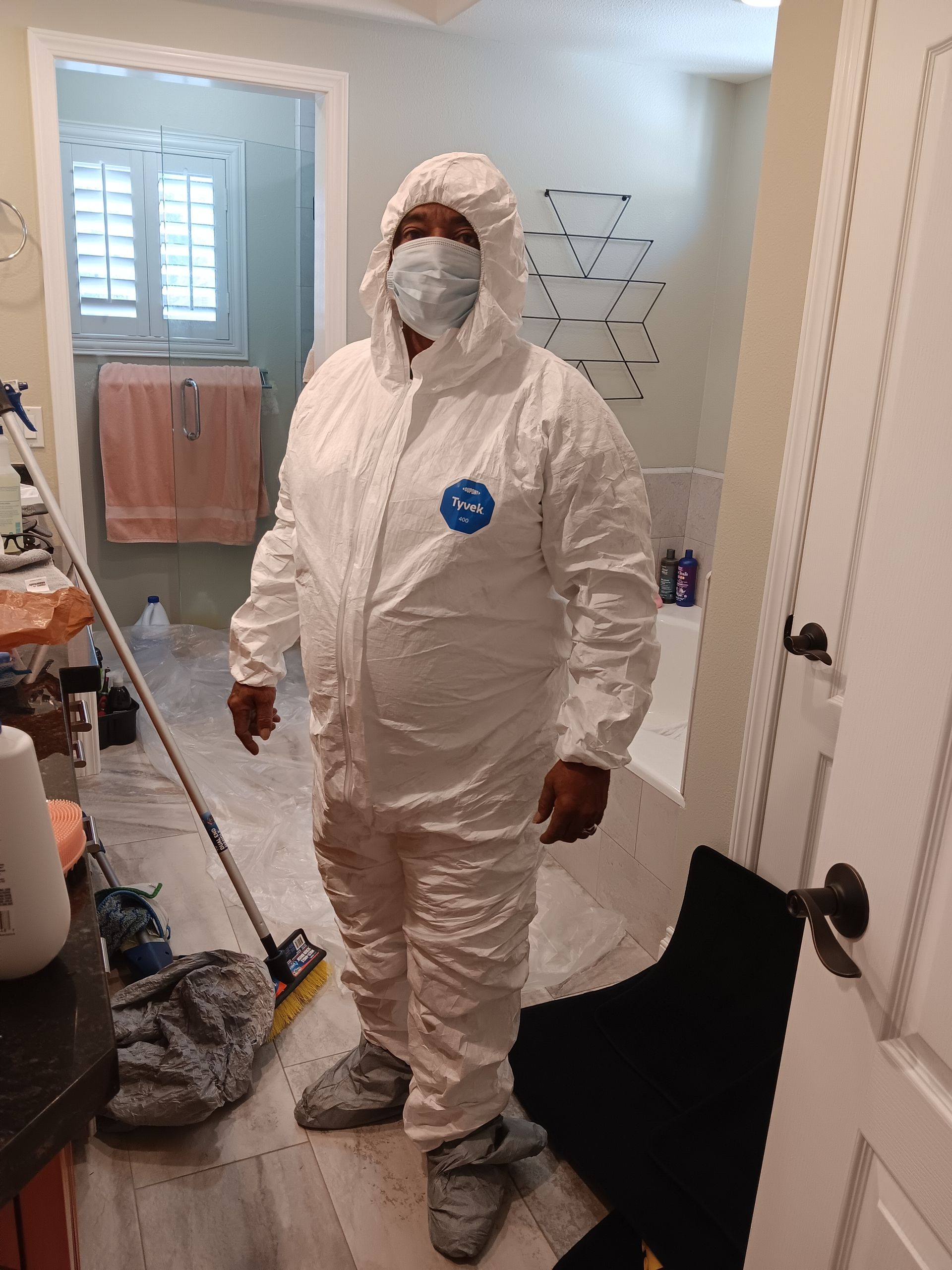 A man in a protective suit is standing in a bathroom with a mop.
