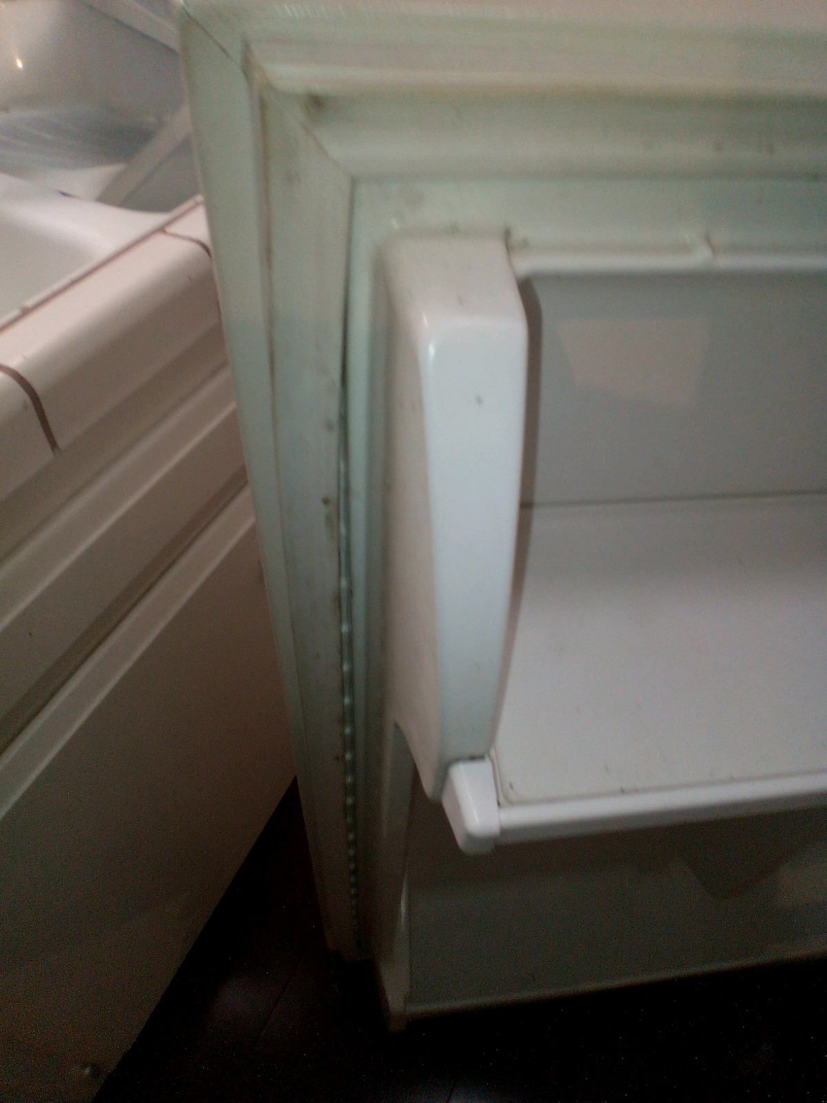 A white refrigerator is sitting next to a bathtub in a bathroom.