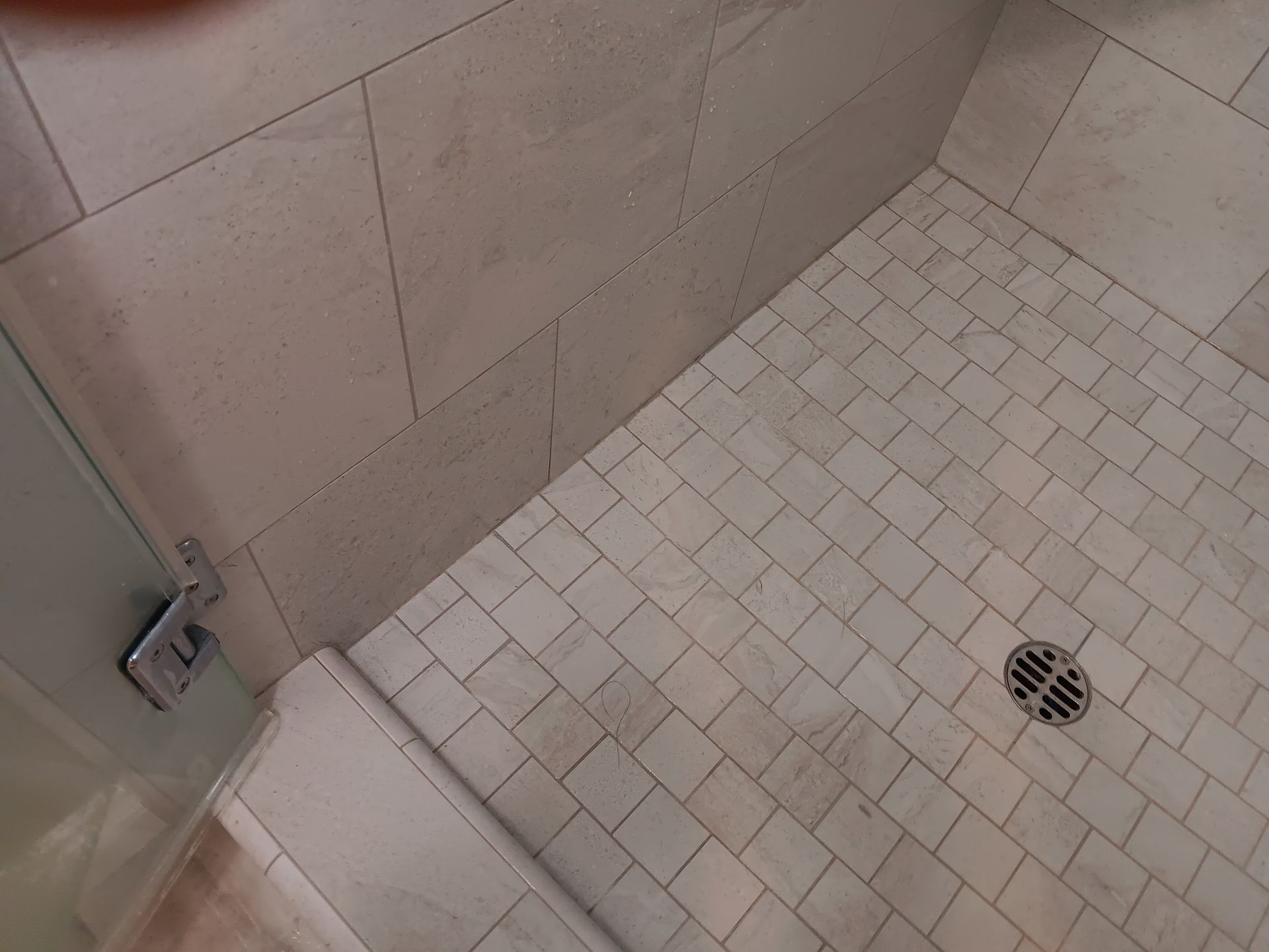 A shower stall with white tiles and a drain on the floor.