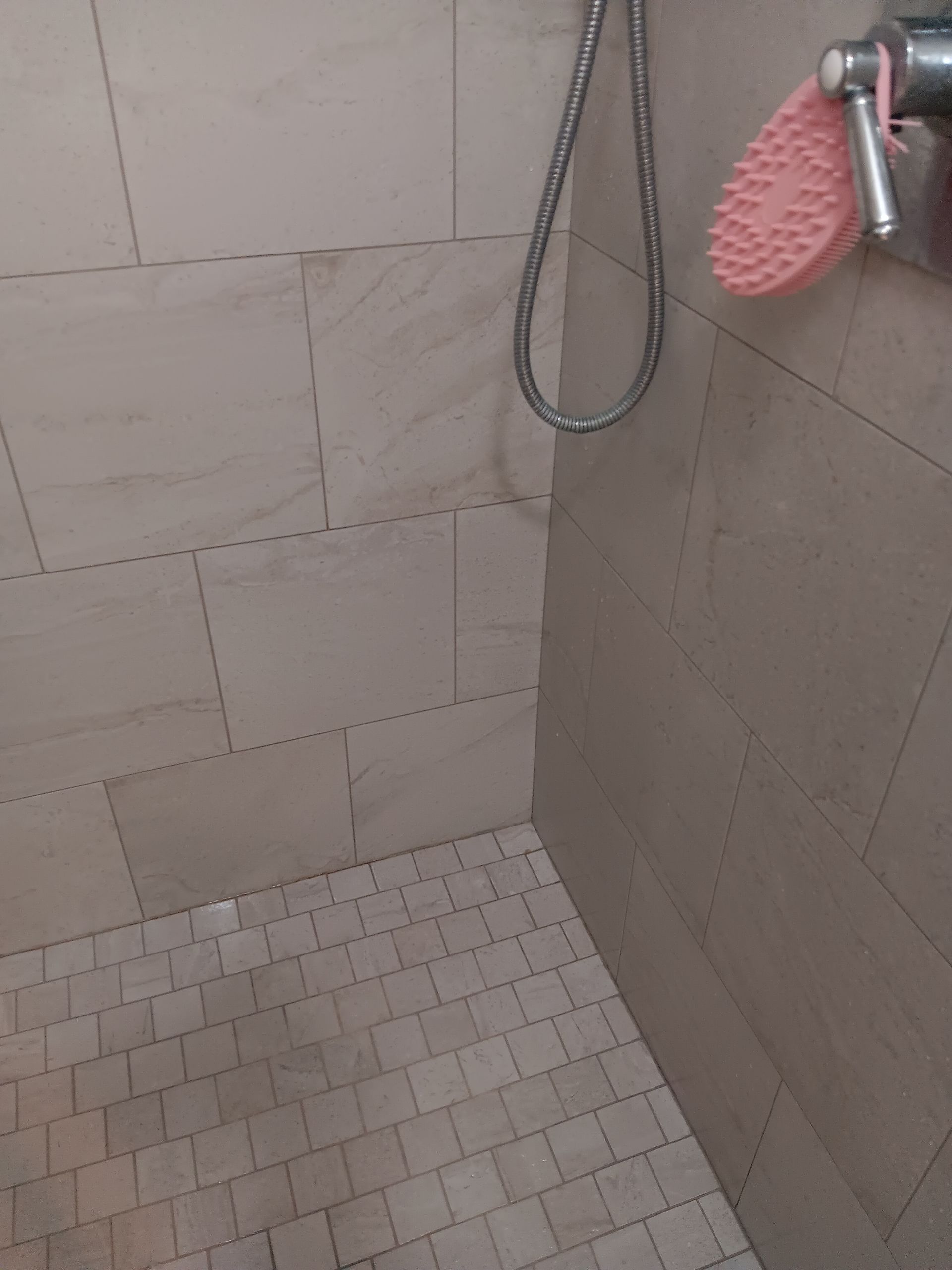 A shower with a pink brush hanging from the shower head.