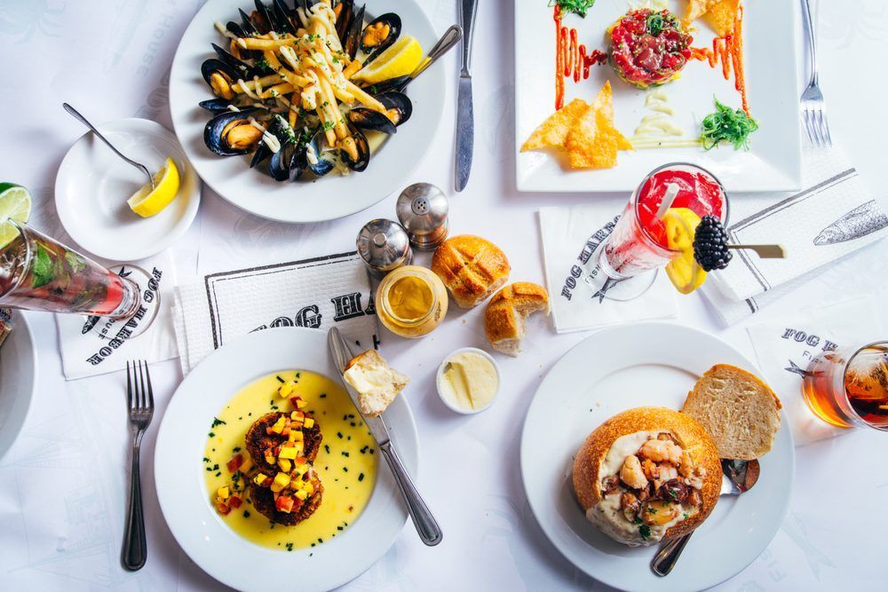 Overhead view of a restaurant table set with various seafood dishes and cocktails.