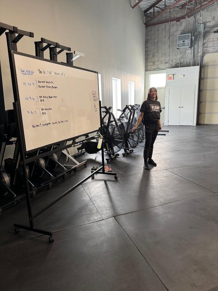 A woman is standing in front of a whiteboard in a gym.