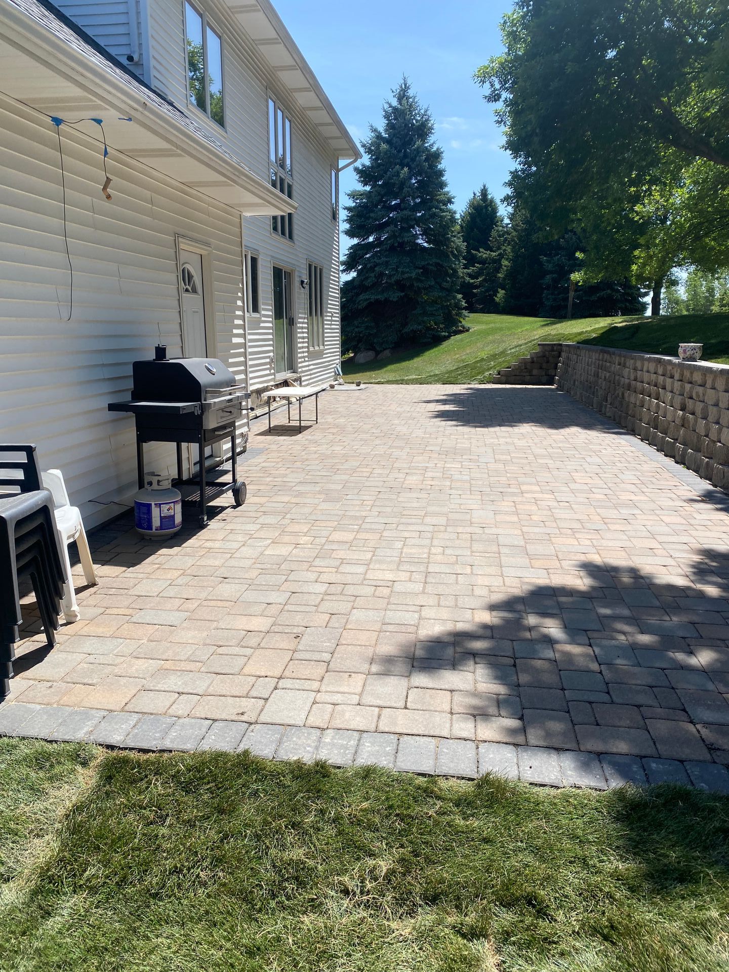 A brick patio with a grill and chairs in front of a house.