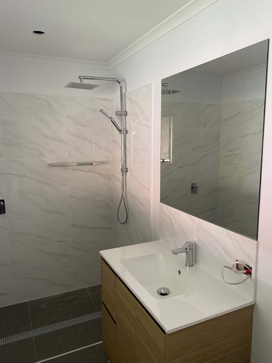 Bathroom With a Large Mirror Above a Wooden Vanity and Sink — Nick Hall Builder in Noosa, QLD