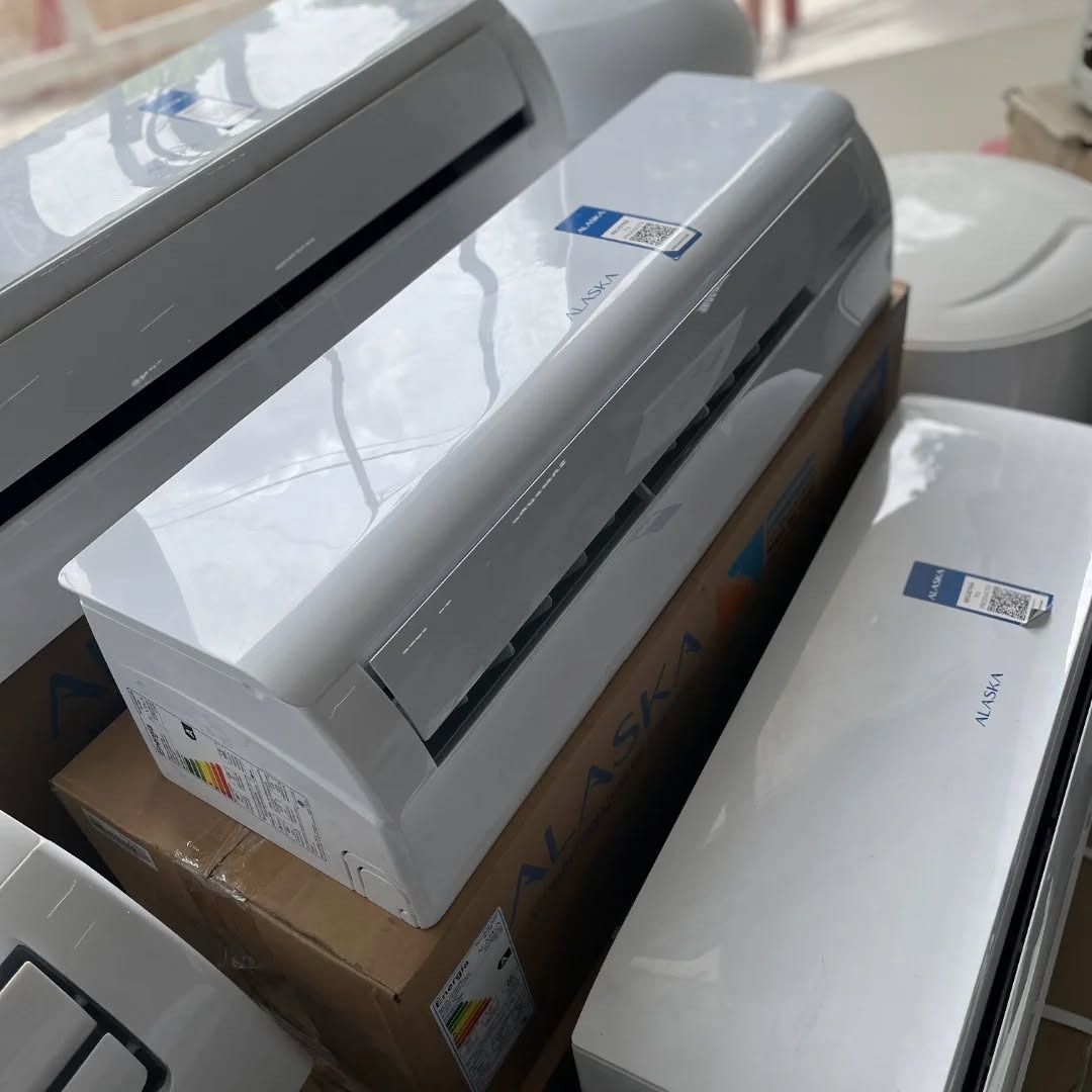 Unidades de aire acondicionado blancas, algunas apiladas, en cajas. Logotipo azul y blanco en la parte frontal.