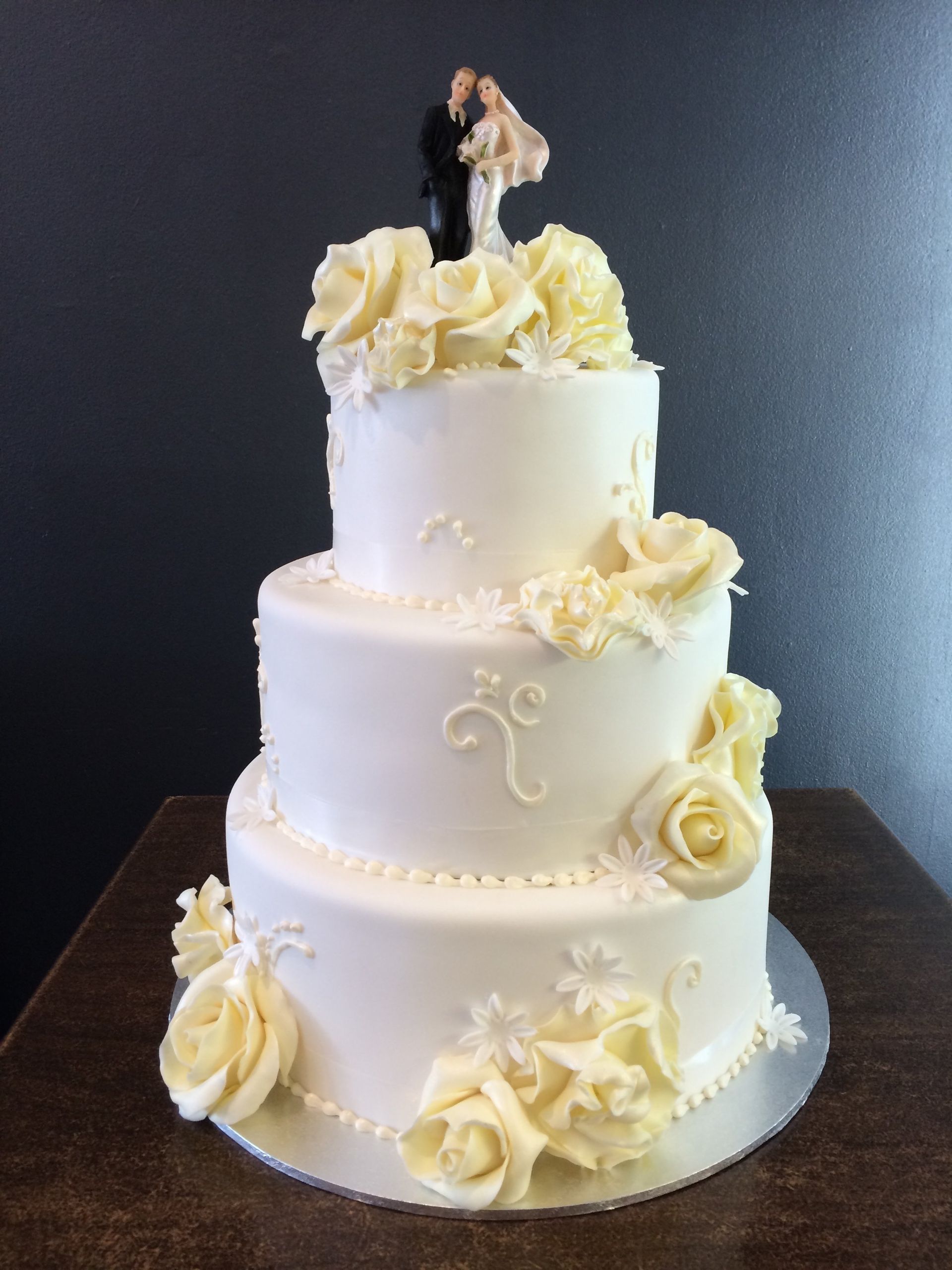 white triple layer cake with rose accents and bride and groom on top