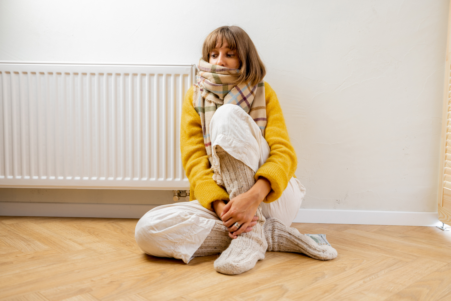 A woman is sitting on the floor in front of a radiator.
