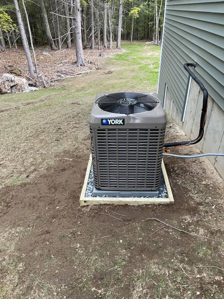 A york air conditioner is sitting in the dirt next to a house.