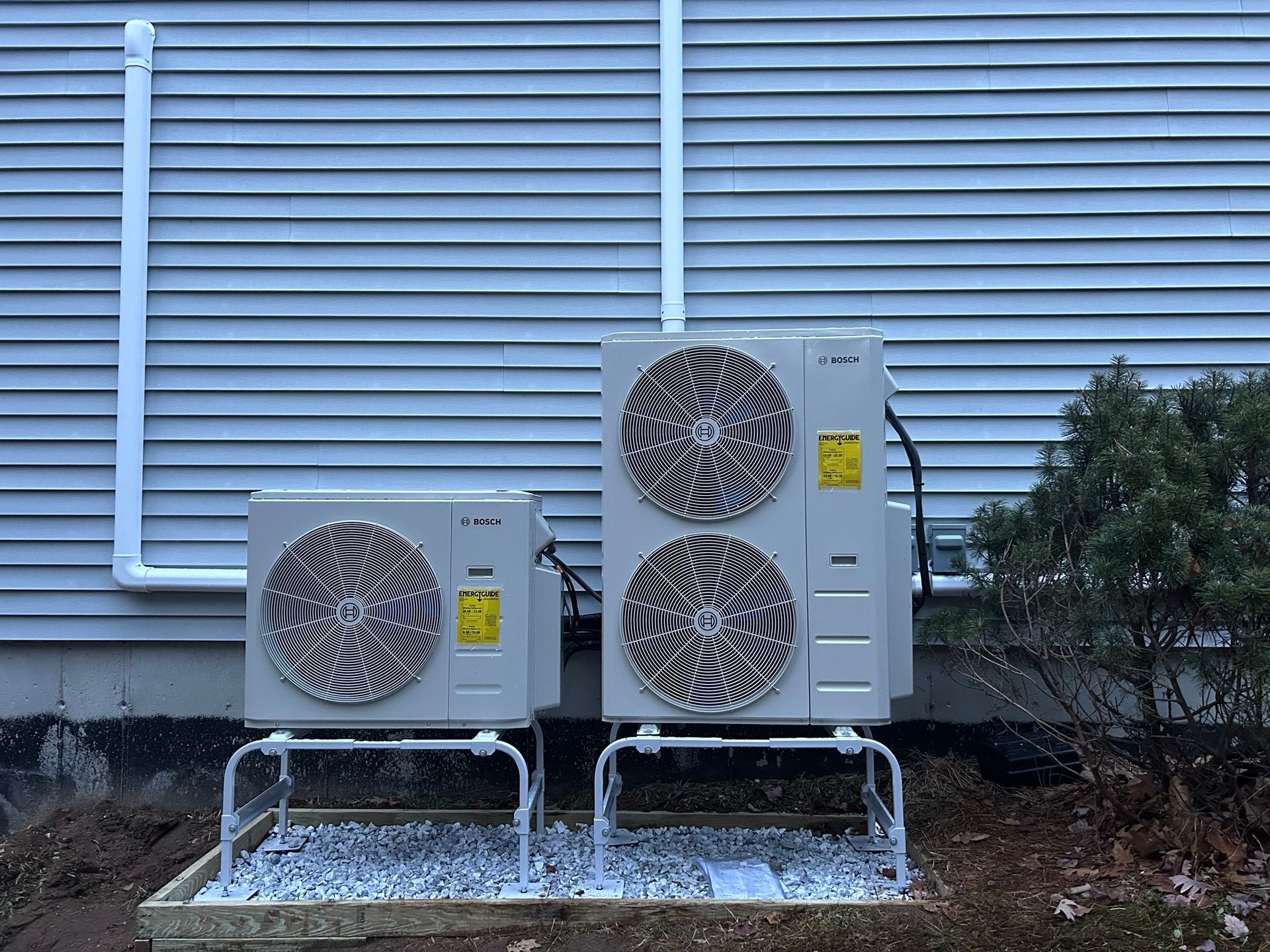 Two air conditioners are sitting outside of a house.