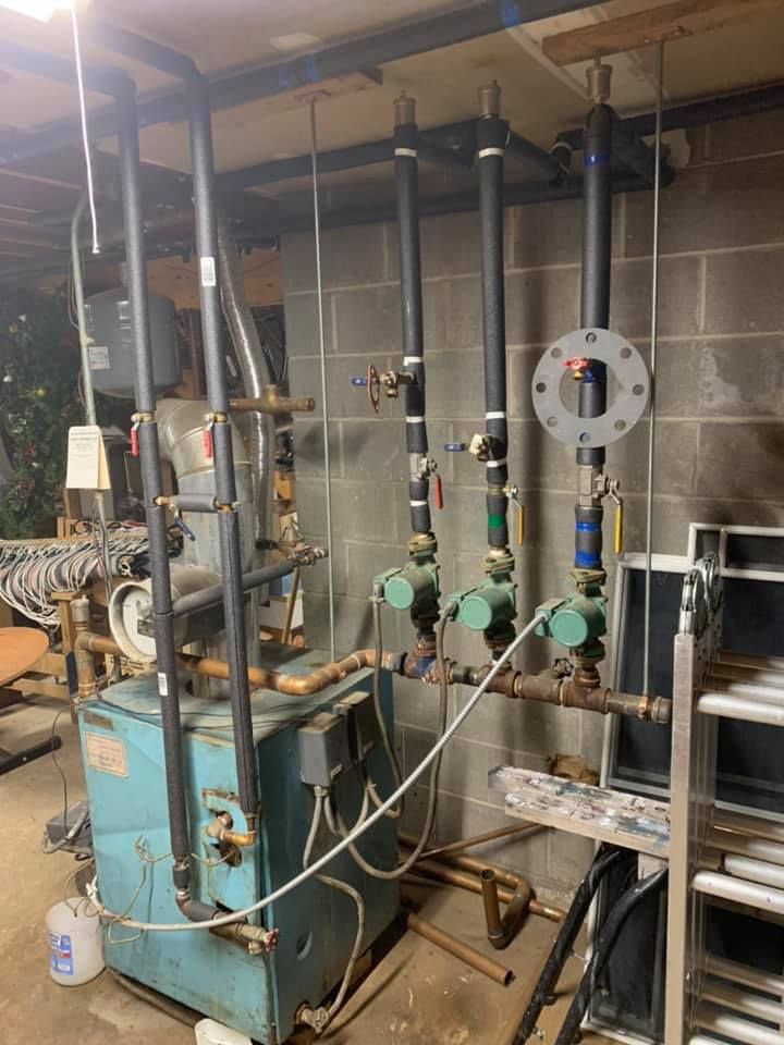 A blue boiler is sitting in a basement next to a bunch of pipes.