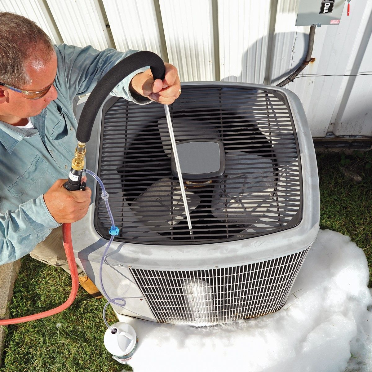A man is cleaning an air conditioner with a hose
