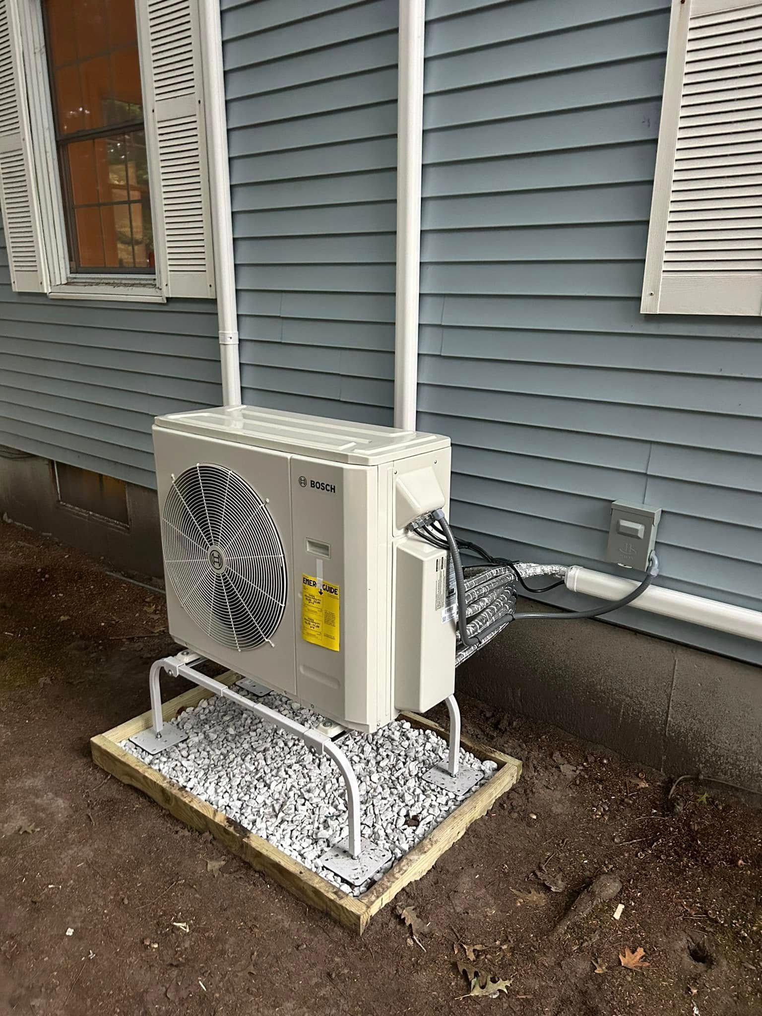 A white air conditioner is sitting on top of a pile of gravel next to a house.