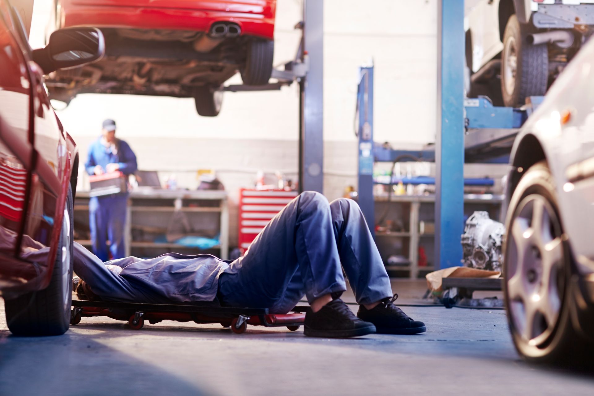 A man is laying on a creeper in a garage under a car.