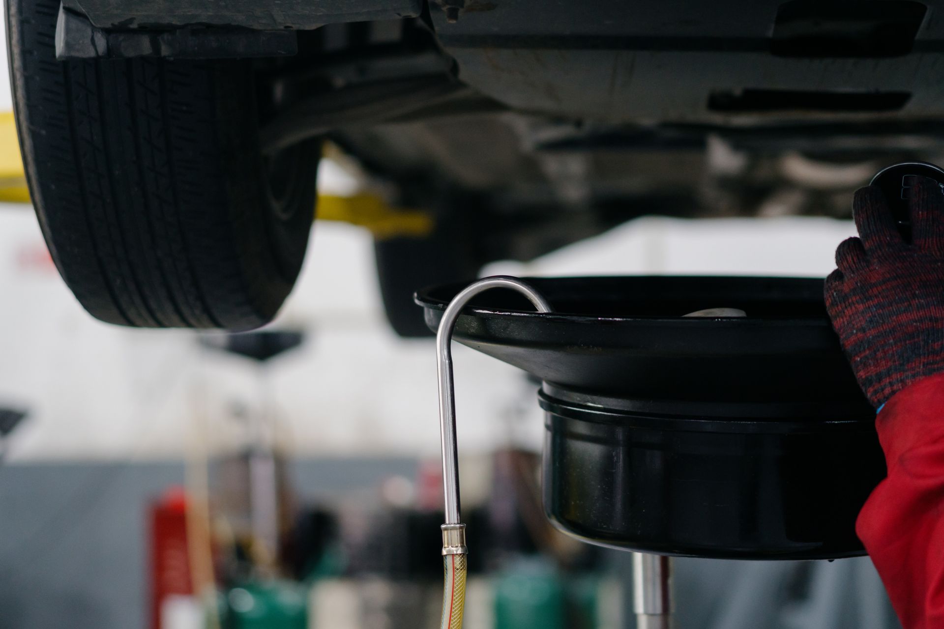 A person is pouring oil into a bucket under a car.