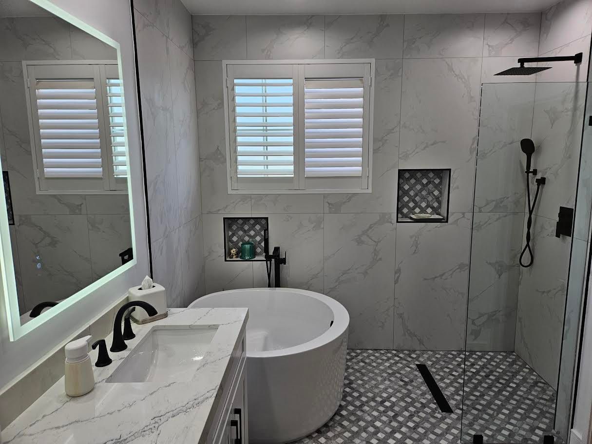 Modern bathroom with a marble vanity, circular soaking tub, glass-enclosed walk-in shower, and white plantation shutters.