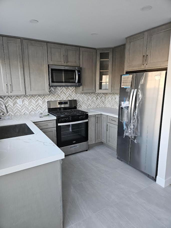 Modern kitchen with light wood cabinets, white countertops, stainless steel appliances, and a chevron-pattern backsplash.