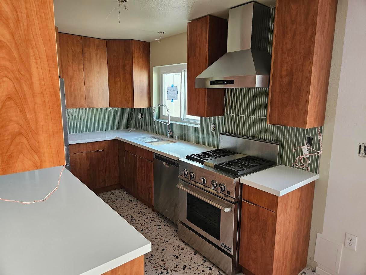 A kitchen with wooden cabinets, stainless steel appliances, a white countertop, and patterned tile backsplash.
