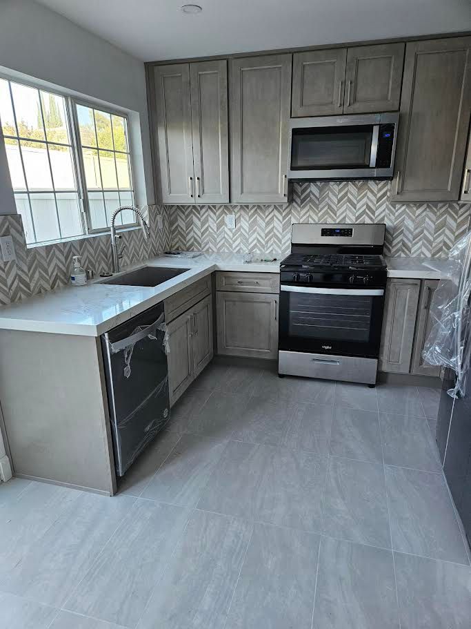 A modern kitchen with light wood cabinets, stainless steel appliances, white countertops, and a herringbone backsplash.